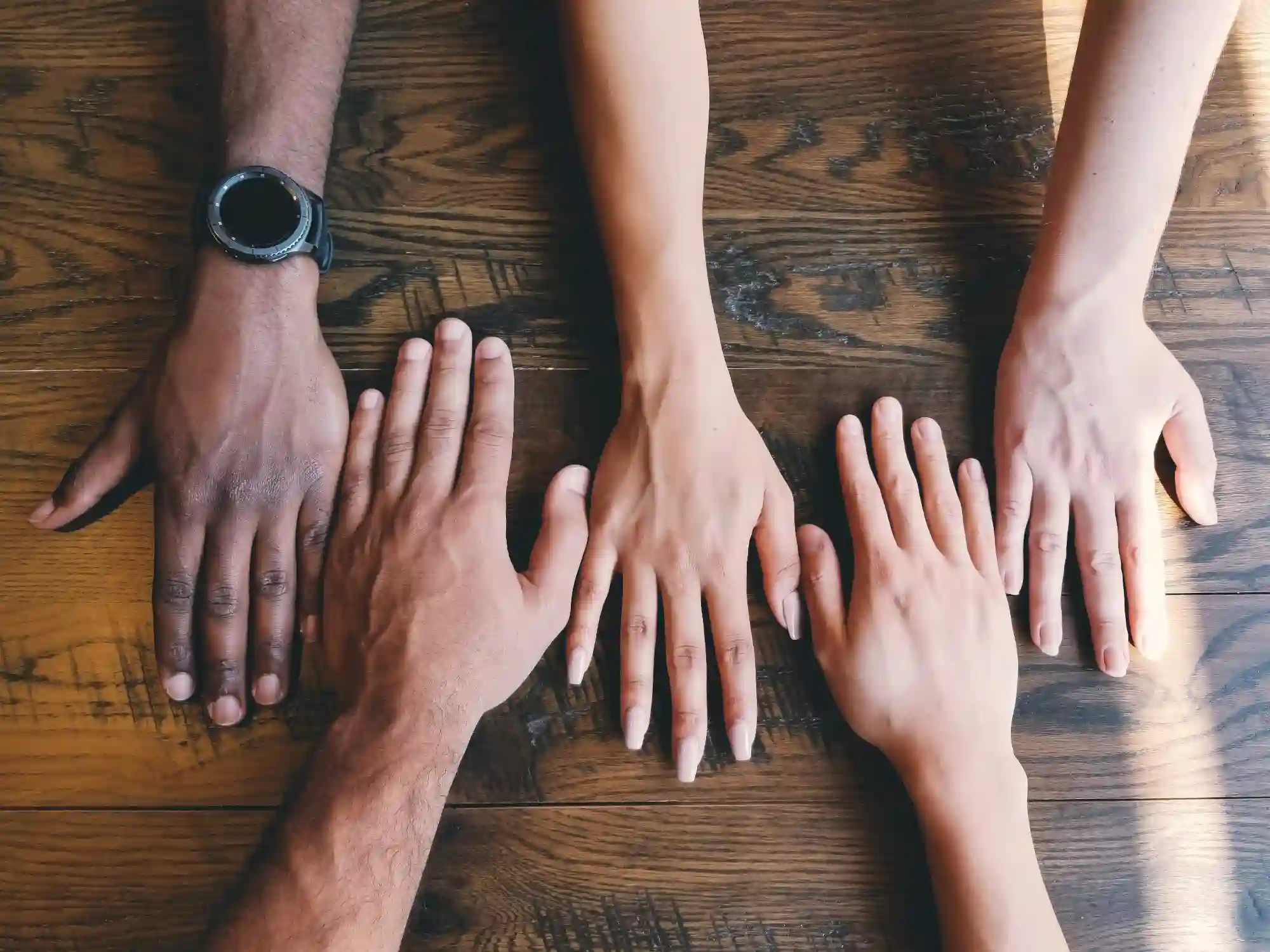 5 Hands Over A Wood Table