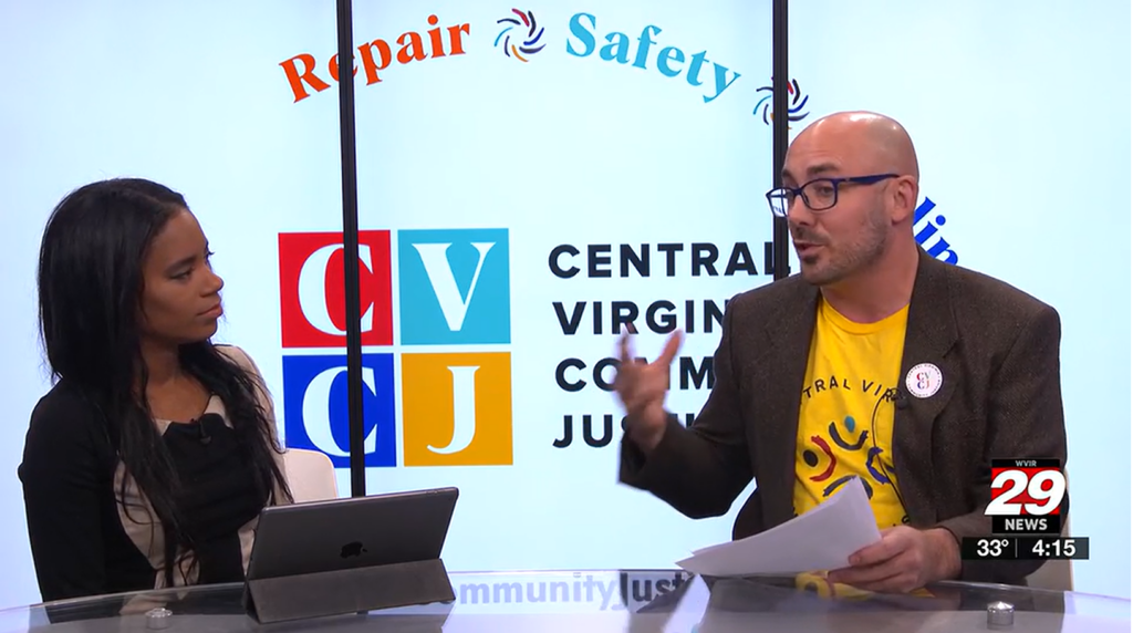 Woman and man speaking in front of a backdrop with CVCJ logo and the words Repair - Safety - Healing